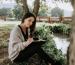 young woman writing on her notebook surrounded by a beautiful view of trees, water, and bridge